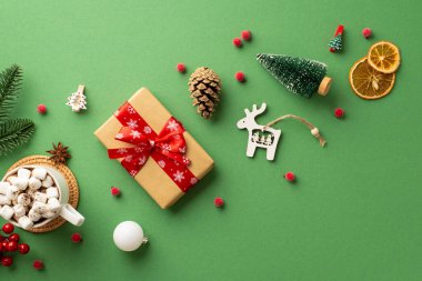 Noel konsepti. Hüner kağıdı hediye kutusu köknar dalı kozalağı bir fincan kakao marshmallow ahşap ren geyiği süsü ökseotu üzü ve izole edilmiş yeşil arka planda kurutulmuş portakal dilimi.