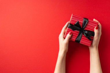 Kara Cuma konsepti. Kadının kırmızı hediye kutusundan siyah kurdeleli ellerinin kopyalanmış kırmızı arka planda olduğu ilk kişi.