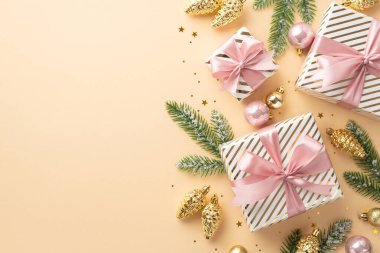 Noel ağacı süslemeleri konsepti. Yay, altın ve pembe takılar içeren hediye kutularının en üstteki fotoğrafı. Çam kozalağı süslemeleri. İzole edilmiş pastel bej arka planda donmuş konfeti köknar dalları.
