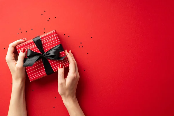 黑色星期五购物的概念 在第一人称头像照片中 女人的手拿着红色礼品盒 上面有黑带蝴蝶结 在孤立的红色背景上带有彩色空间 — 图库照片