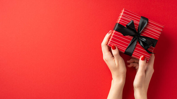 Black friday concept. First person top view photo of girl's hands holding red giftbox with black ribbon bow on isolated red background with copyspace