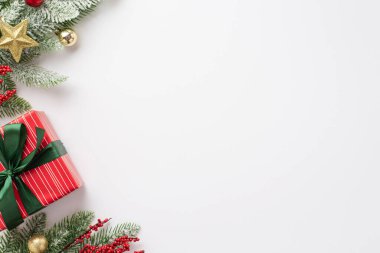 Yeni yıl konsepti. Kardaki çam dalının üst görüntüsü mücevherlerle süslenmiş yıldız süsü ökseotu üzümleri ve izole edilmiş beyaz arka planda yeşil kurdeleli kırmızı hediye kutusu.