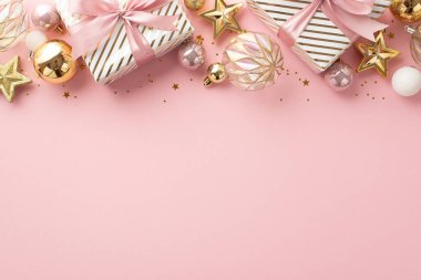 Noel arifesi kavramı. Kurdeleli şık hediye kutularının üst görünümü beyaz şeffaf pembe takılar altın yıldız süslemeleri ve izole edilmiş pastel pembe arka planda boş alan konfetileri.