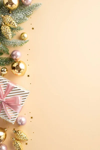 New Year decorations concept. Top view vertical photo of present box gold and pink baubles pine cone ornaments fir branch in hoarfrost and confetti on isolated pastel beige background with copyspace