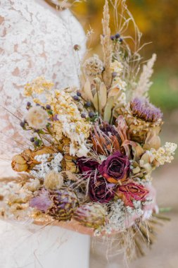 Gelinin ellerinde bir buket kurumuş kır çiçeği. Yaklaş.