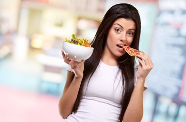 kadın bir parça pizza yemek ve salata kasesi holding