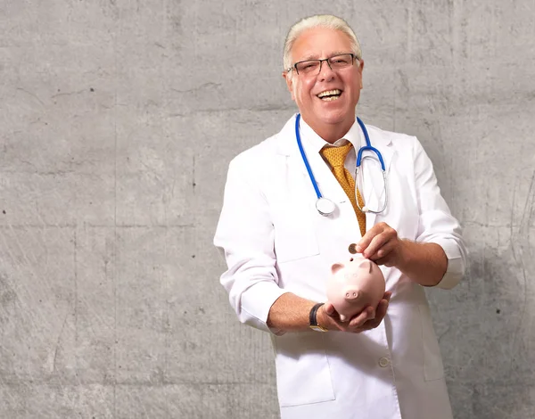 Male Doctor Putting Coins In A Piggy Bank — Stock Photo, Image