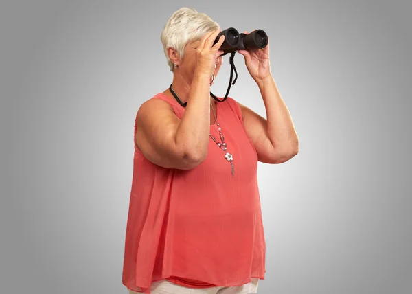 Une femme âgée regardant à travers les jumelles — Photo