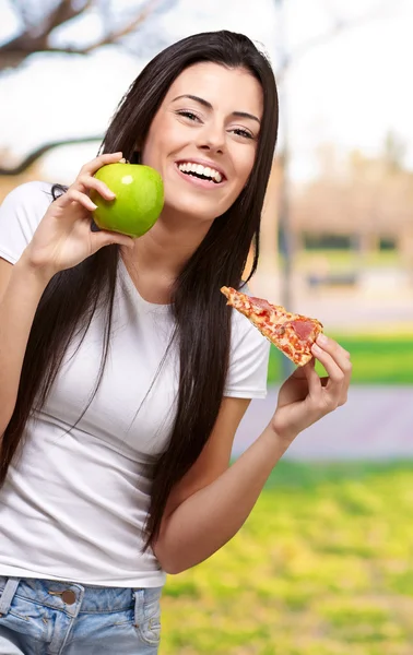 Feminino segurando um pedaço de pizza e uma maçã — Fotografia de Stock