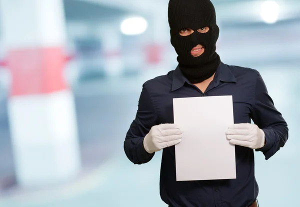 Man wearing a robber mask showing a blank paper — Stock Photo, Image