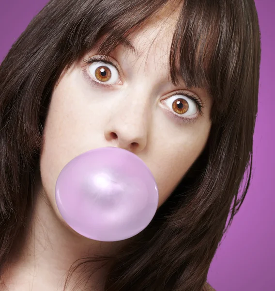 Young girl with a pink bubble of chewing gum against a pink back — Stockfoto
