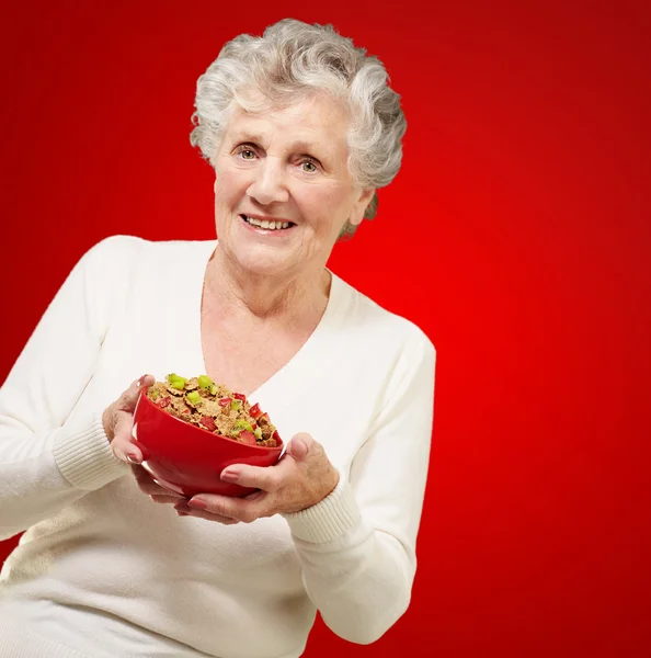 Retrato de mulher idosa saudável segurando tigela de cereais sobre b vermelho — Fotografia de Stock