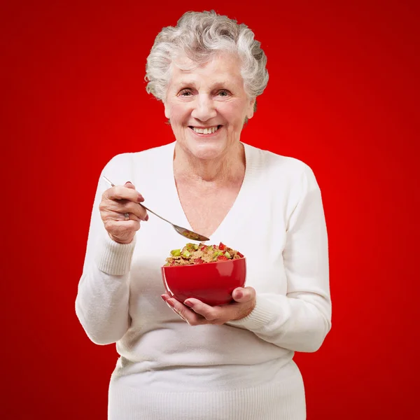 Portrait of senior woman holding a cereals bowl against a red ba — Stock Photo, Image