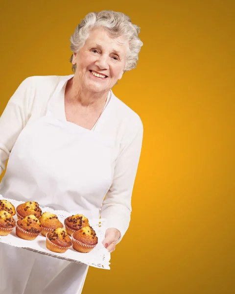 Retrato de cocinera mujer mayor sosteniendo una bandeja de magdalenas de chocolate o — Foto de Stock