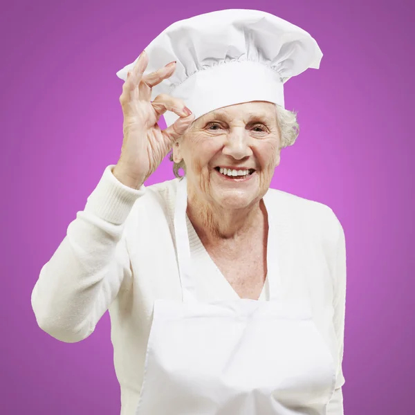 Anziano donna cuoco facendo un ottimo simbolo contro un rosa backg — Foto Stock