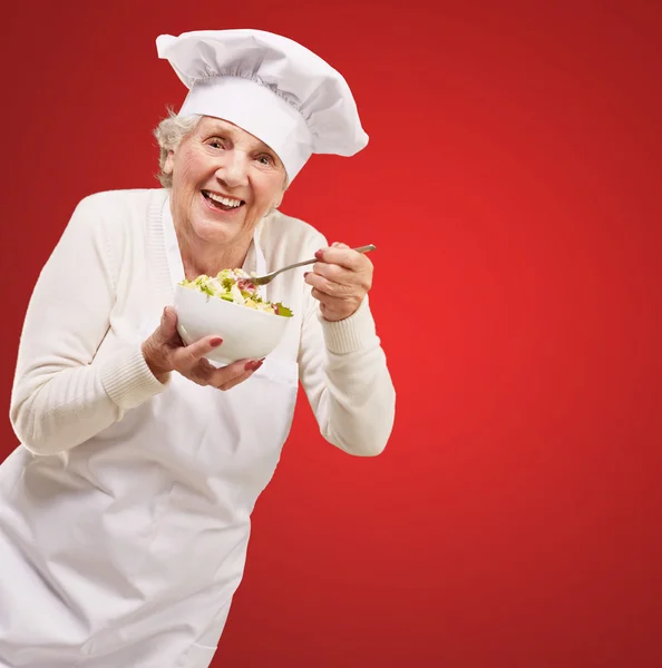 Porträt einer Seniorin, die Salat über Rot isst — Stockfoto