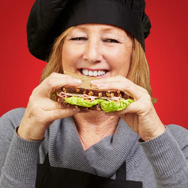 Μέσης ηλικίας γυναίκα τρώει σάντουιτς φυτικά πέρα από το κόκκινο υπόβαθρο — Φωτογραφία Αρχείου