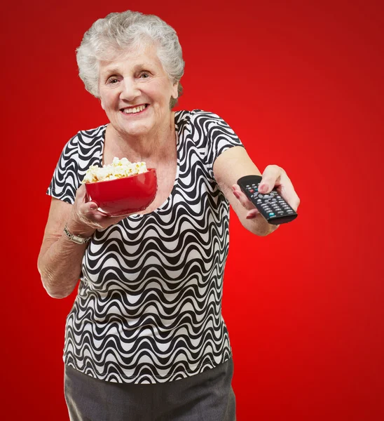 Portrait of happy senior woman looking the tv over red backgroun — Stock Photo, Image