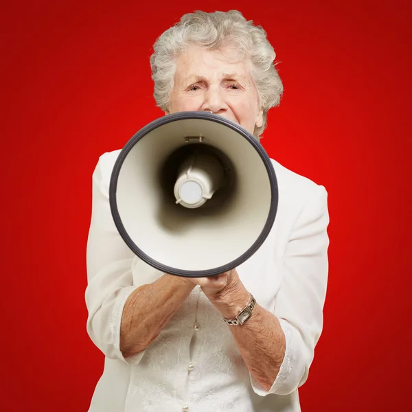 Portrait de femme âgée criant avec mégaphone sur fond rouge — Photo