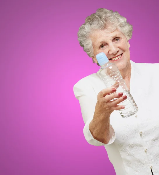 Portret zdrowe kobiety starszy trzyma butelkę wody nad pur — Zdjęcie stockowe