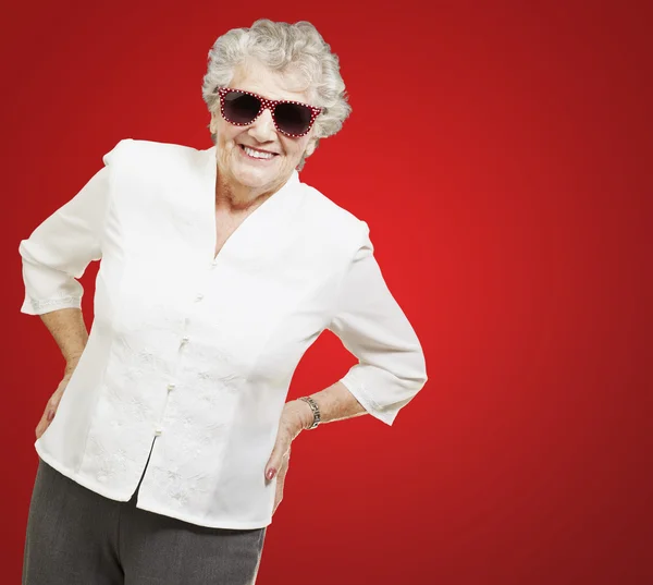 Portrait of senior woman standing wearing sunglasses over red ba — Stock Photo, Image