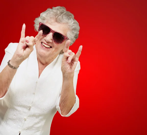 Портрет счастливой пожилой женщины, изображающей рок-символ на красной спине — стоковое фото
