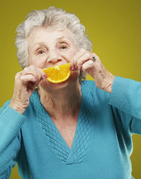 Portrait of senior woman holding a orange slice in front of her — Stock Photo, Image