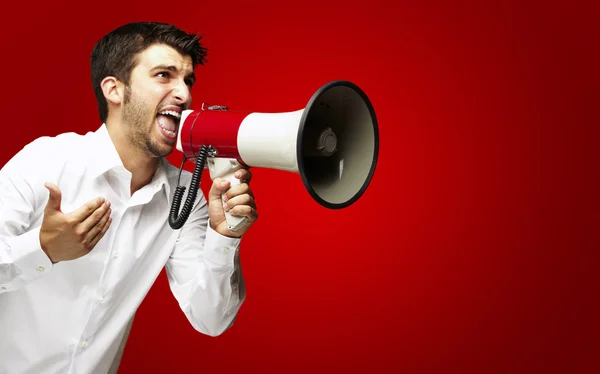 Retrato del joven gritando con megáfono sobre fondo rojo — Foto de Stock