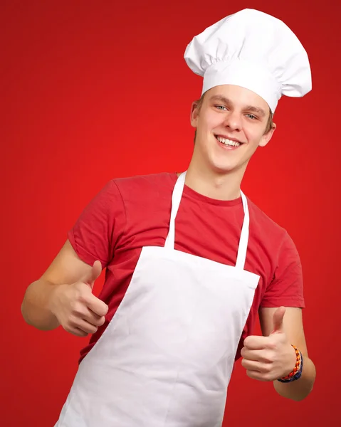 Retrato de jovem cozinheiro fazendo símbolo de sucesso contra um ba vermelho — Fotografia de Stock