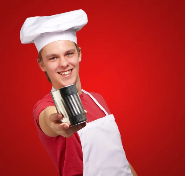 Retrato del joven cocinero sosteniendo una lata de metal sobre la espalda roja —  Fotos de Stock