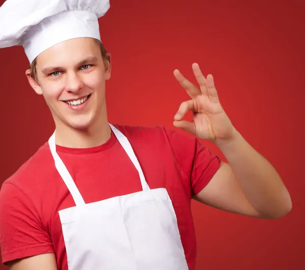Νέοι μάγειρας άνθρωπος κάνει καλό σύμβολο πάνω από το κόκκινο φόντο电子邮件的笔记本 — Φωτογραφία Αρχείου