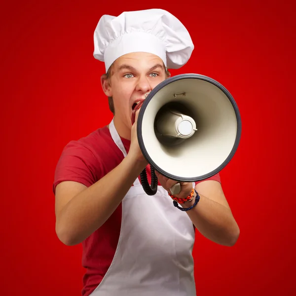 Retrato del joven cocinero gritando con megáfono sobre bac rojo — Foto de Stock