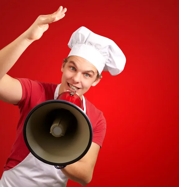 Retrato de homem cozinheiro feliz gritando usando megafone sobre bac vermelho — Fotografia de Stock