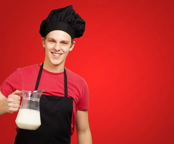 Potret seorang juru masak muda memegang botol susu di atas latar belakang merah — Stok Foto