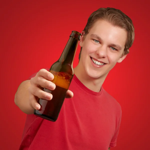 Retrato de jovem segurando cerveja sobre fundo vermelho — Fotografia de Stock