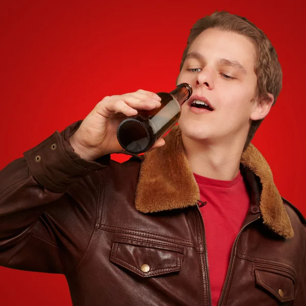 Portrait of young man drinking beer against a red background — Stock Photo, Image