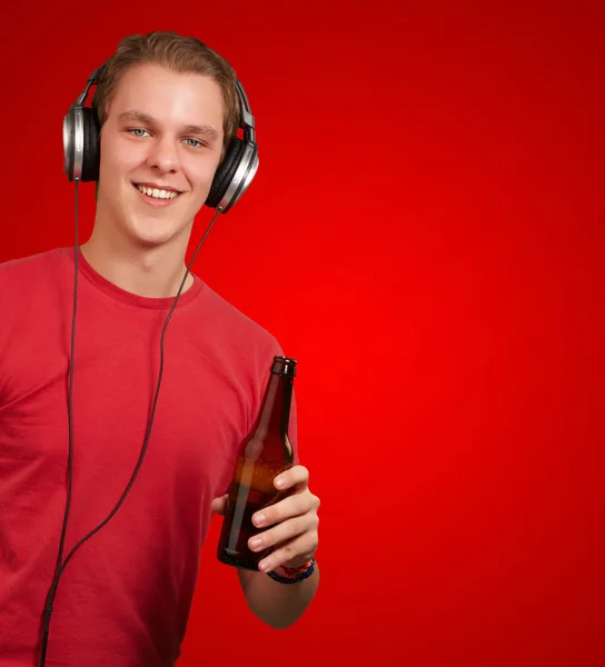 Ritratto di un giovane che ascolta musica e tiene la birra sul rosso — Foto Stock