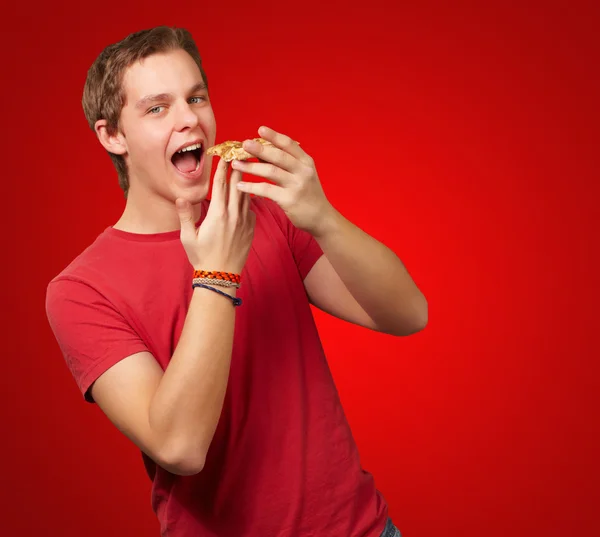 Портрет молодого человека, поедающего пиццу на красном фоне — стоковое фото