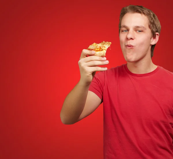 Retrato de jovem comendo pizza porção sobre vermelho backgorund — Fotografia de Stock