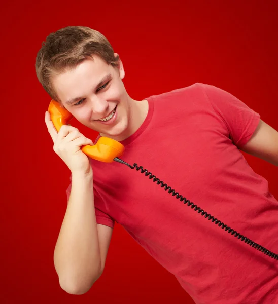 Портрет молодого человека разговаривающего по винтажному телефону за красной спиной — стоковое фото