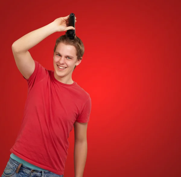 Portrait de jeune homme coupant ses cheveux sur fond rouge — Photo