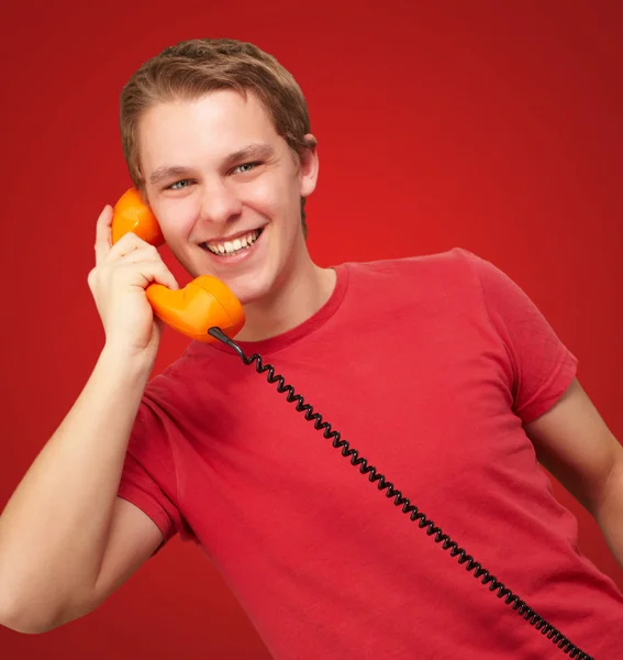 Portrait of young man talking with vintage telephone over red ba Stock Picture