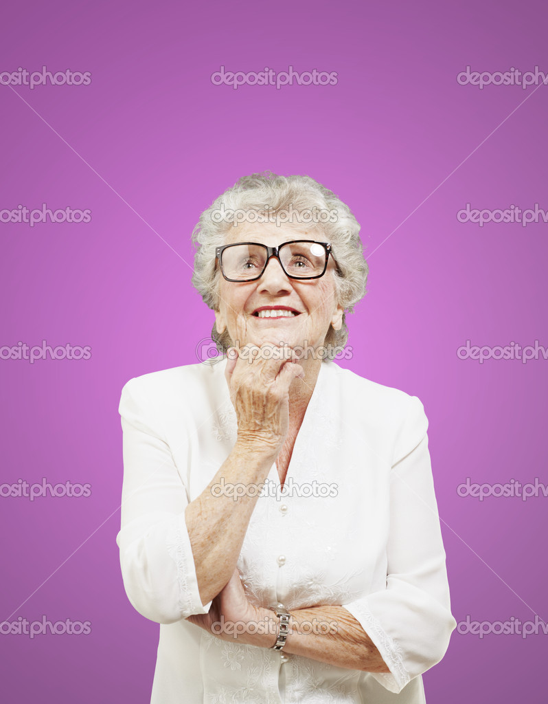 Portrait of senior woman thinking and looking up over pink backg