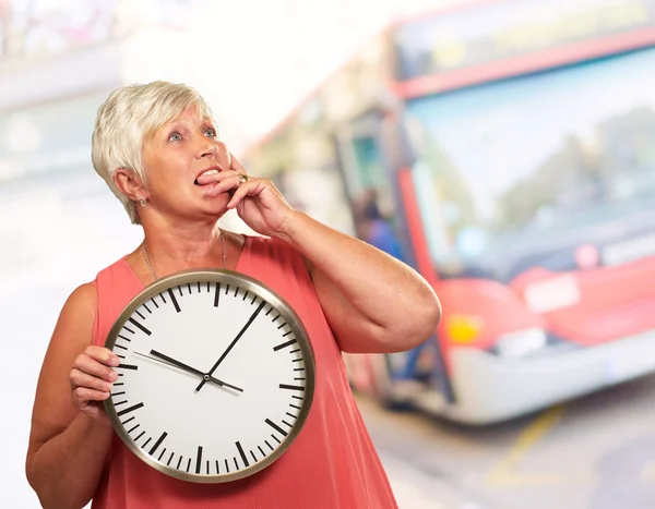 Senior vrouw houden een klok en denken — Stockfoto