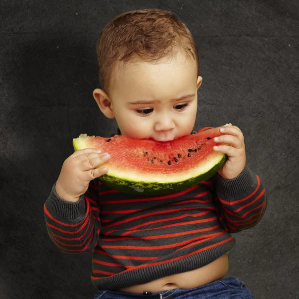 Portrait of a handsome kid biting a watermelon against a grunge — Stock Photo, Image