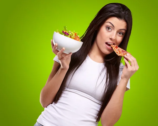 Frau isst ein Stück Pizza und hält eine Salatschüssel in der Hand — Stockfoto