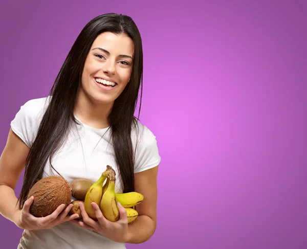 Portrait of young woman holding tropical fruits against a purple — Stock Photo, Image