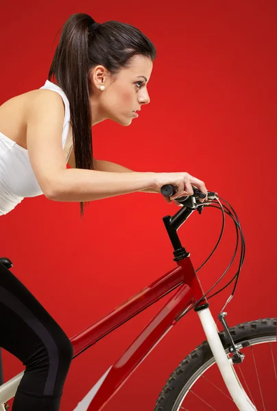 Jovem menina desportiva ciclismo sobre fundo vermelho — Fotografia de Stock