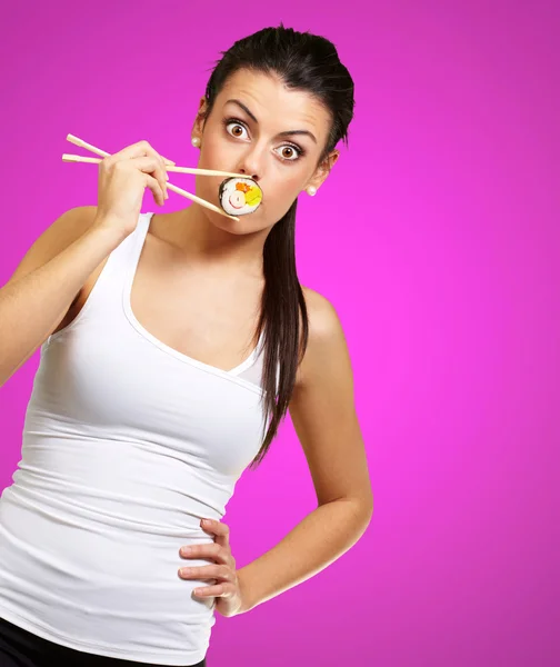 Junge Frau bedeckt ihren Mund mit einem Sushi-Stück gegen ein rosa — Stockfoto