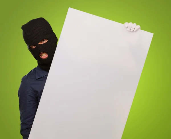 Man wearing mask holding a blank card against a green background — Stock Photo, Image